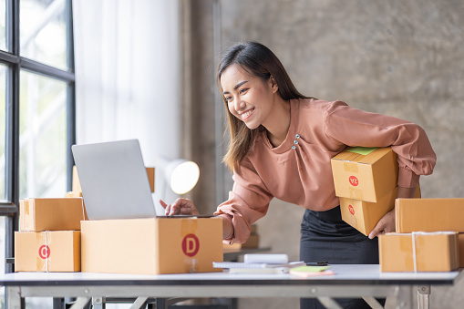 PME Vendeur en ligne Jeune femme asiatique travaillant sur un ordinateur portable et une boîte vérifiant la commande en ligne, vérifiant les marchandises stockées livraison colis postal. Femme asiatique startup PME petite entreprise à domicile bureau