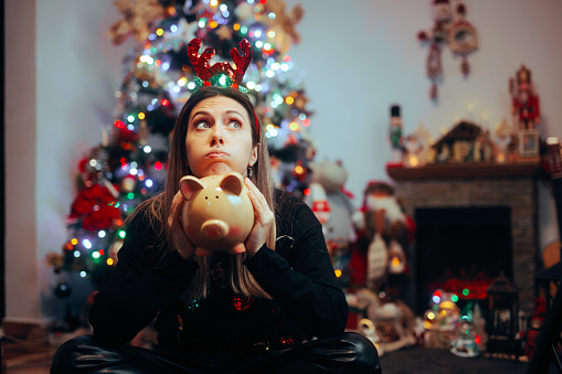 Image d'une femme avec une tirelire et un sapin de Noël derrière elle.
