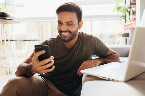 Homme joyeux utilisant un smartphone et un ordinateur portable à la maison