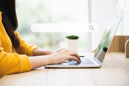 Femme utilisant un ordinateur portable sur un bureau en bois. Elle travaille à la maison