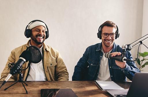 Présentateurs radio masculins s'amusant lors d'une émission en direct. Deux hommes souriant joyeusement lors de l'enregistrement d'une émission audio dans un studio. Des créateurs de contenu collégial co-animant un podcast sur Internet.