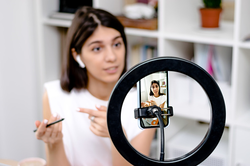 Une fille d'influence, blogueuse, parlant smartphone, enregistrant en direct un blog vidéo sur un réseau social à la maison.concept de diffusion en direct des médias sociaux.focus sur le téléphone, la fille en arrière plan dans un flou.