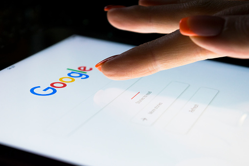 La main d'une femme touche l'écran d'une tablette informatique iPad Pro la nuit pour effectuer une recherche sur le moteur de recherche Google. Google est le moteur de recherche Internet le plus populaire au monde. Photo prise dans les bureaux de l'entreprise.