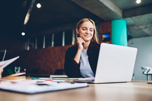 La femme graphiste à succès regarde un tutoriel sur les idées créatives à l'ordinateur portable pendant le processus de travail au bureau. Étudiante positive aux cheveux blonds lisant les nouvelles du monde des affaires sur un netbook.