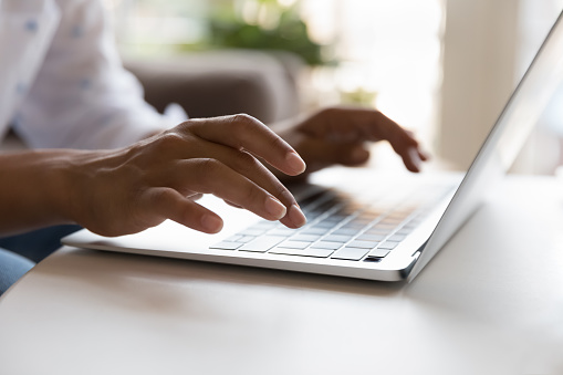 Jeune femme utilisant un ordinateur portable et tapant sur le clavier. Les mains d'une femme en gros plan. Propriétaire décontracté, pigiste, écrivain travaillant à la table, assis sur le canapé de la maison, en train de discuter. Prise de vue recadrée