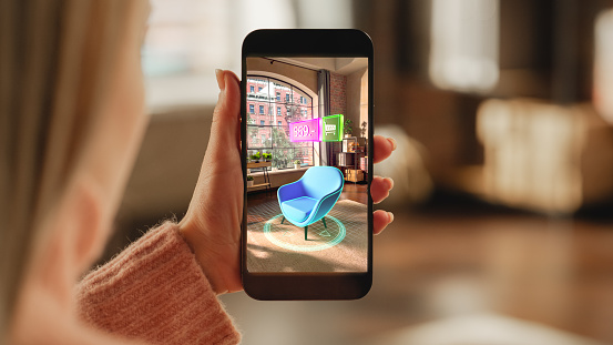 Vue de dessus d'une main féminine tenant un smartphone avec un écran de réalité augmentée montrant une chaise. Femme faisant des achats en ligne et vérifiant ses options dans une situation réelle à distance.