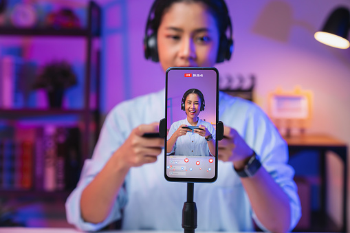 Vlogger live streaming podcast review on social media, Young Asian woman use microphones wear headphones with smartphone record video. Concept de créateur de contenu.