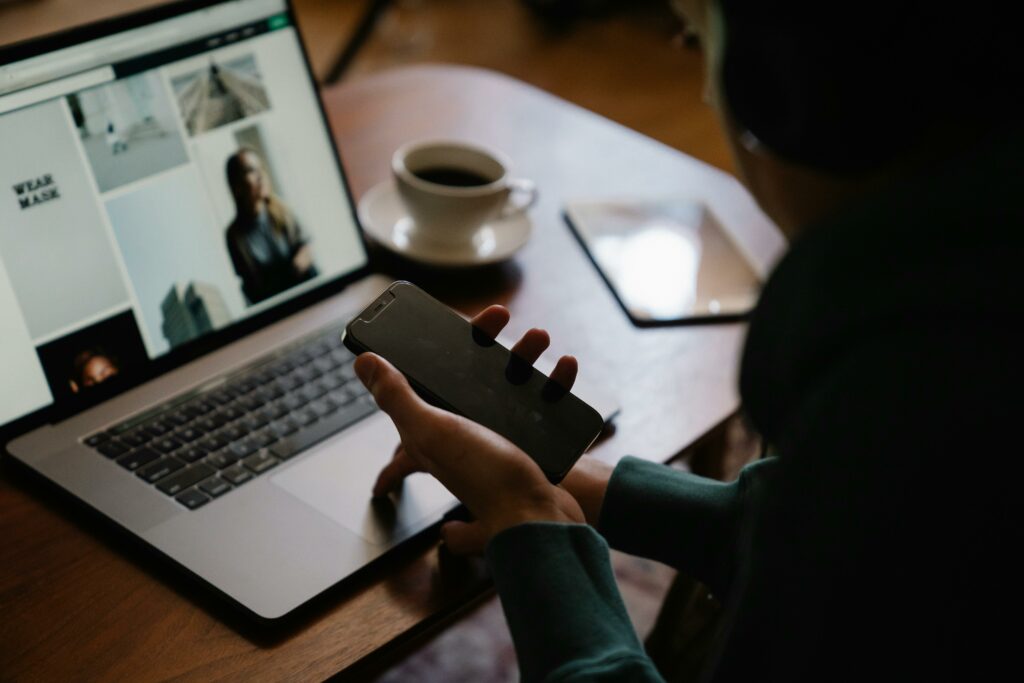 a person holding a phone and looking at a laptop screen