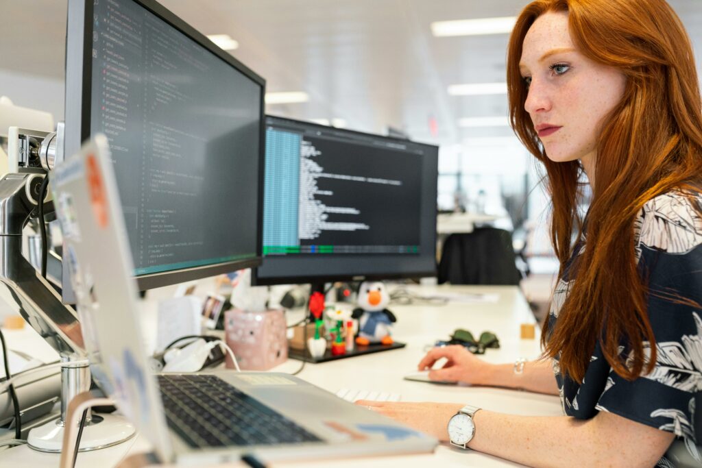 a woman sitting at a desk with two computers