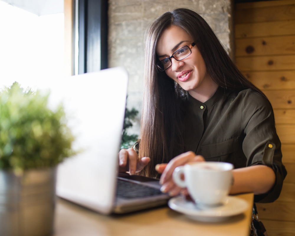 a woman sitting at a table with a laptop and a cup of coffee