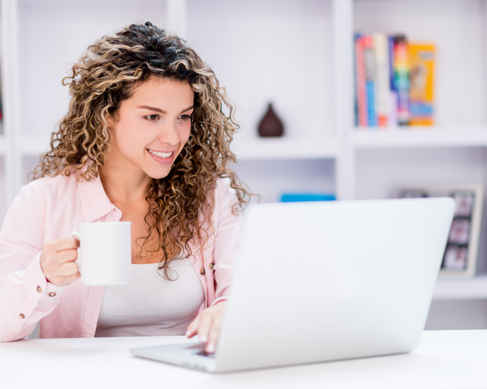 a woman holding a cup and typing on a laptop