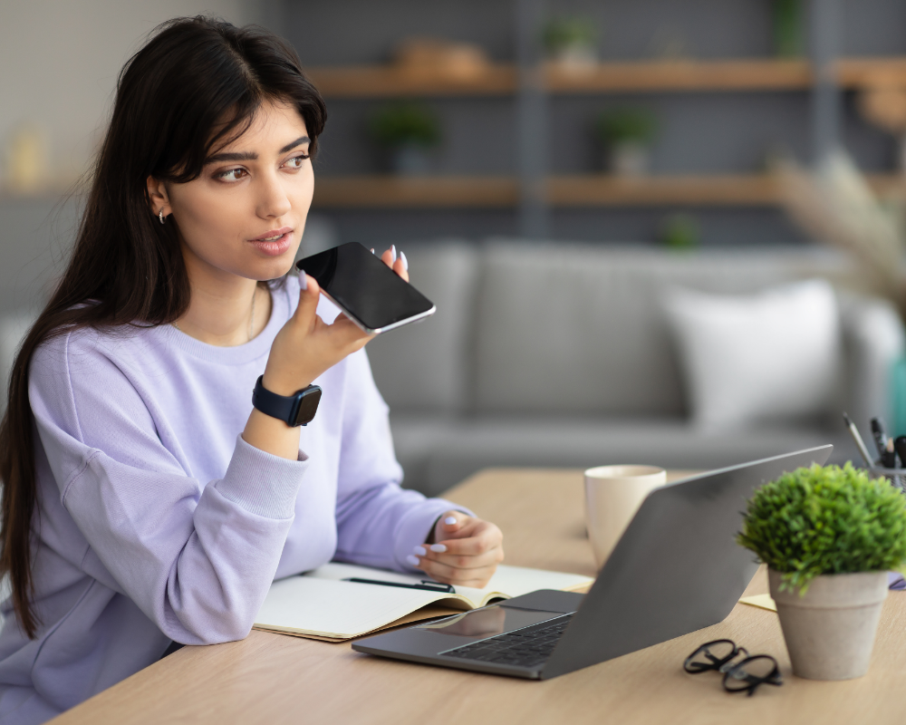 a woman sitting at a table with a laptop and a phone